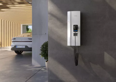 Wallbox hängt nach der Anmeldung im Carport bereit zum Laden des E-Autos, das im Hintergrund parkt.